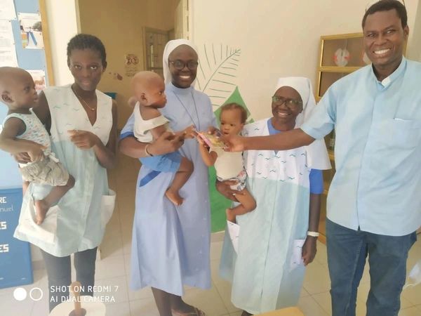 Healthcare workers and nuns holding babies in a clinic, smiling and interacting.