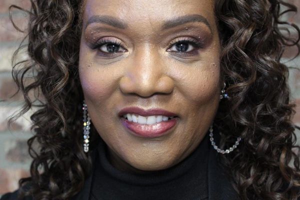 Close-up of a smiling woman with curly hair and hoop earrings.