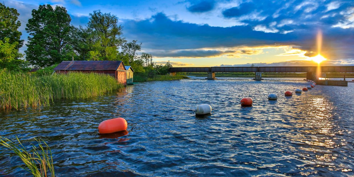 Sunset over a river with a bridge and boathouses.