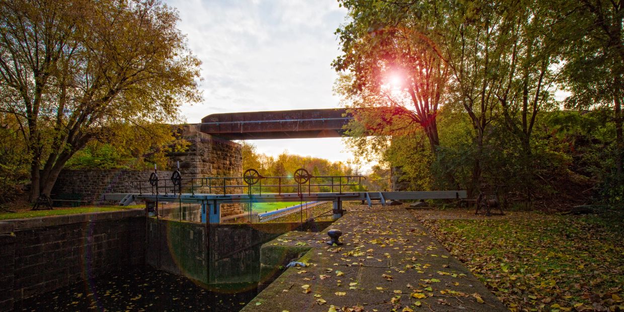Sunlight through trees near an old canal lock and bridge.