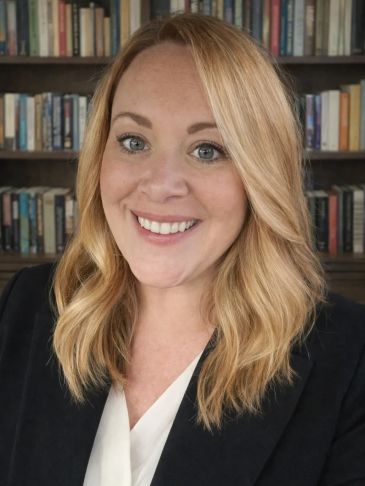 Smiling woman with blonde hair in front of a bookshelf.