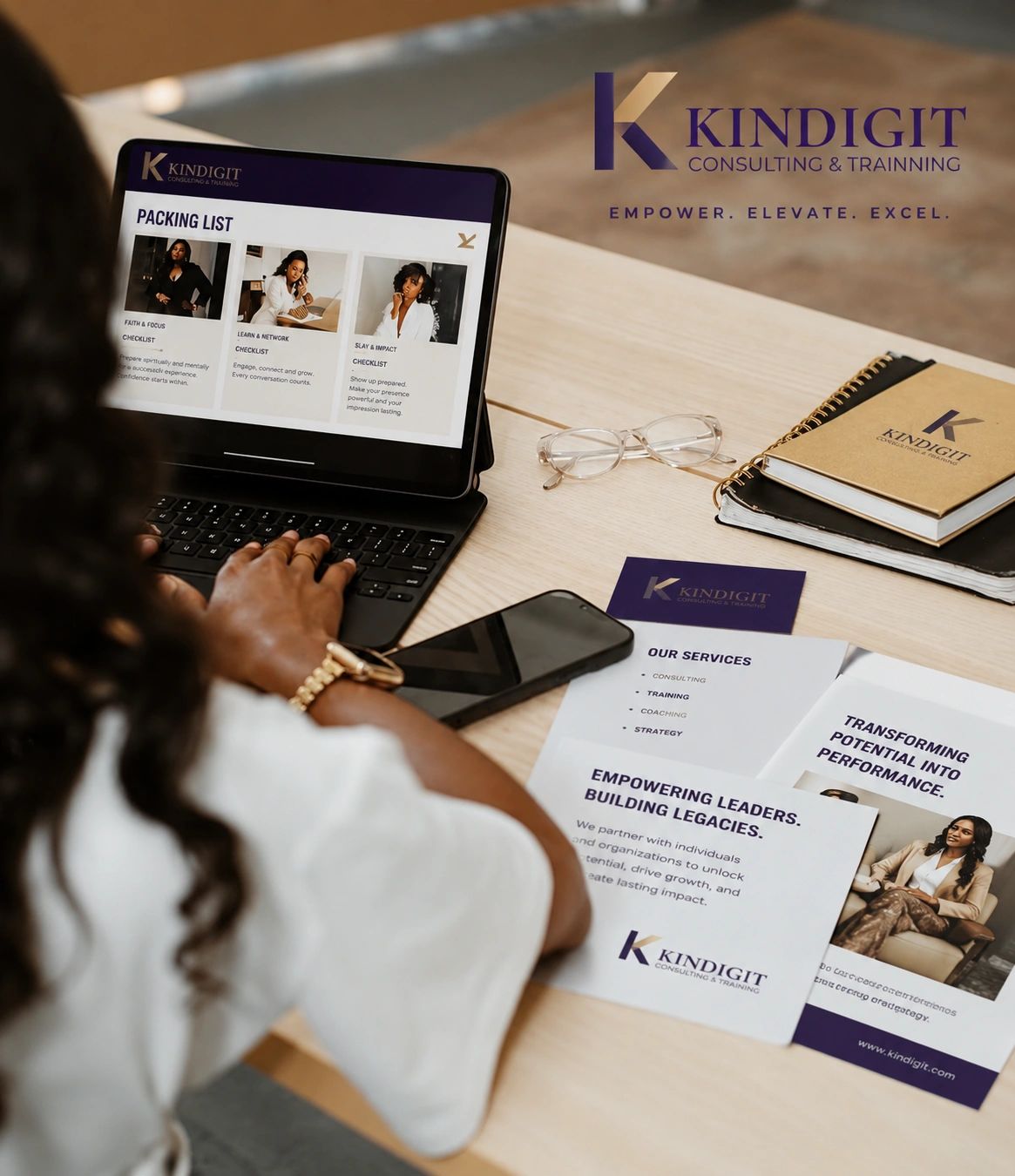 Person working on a laptop with Kindigit Consulting & Training materials on a desk.