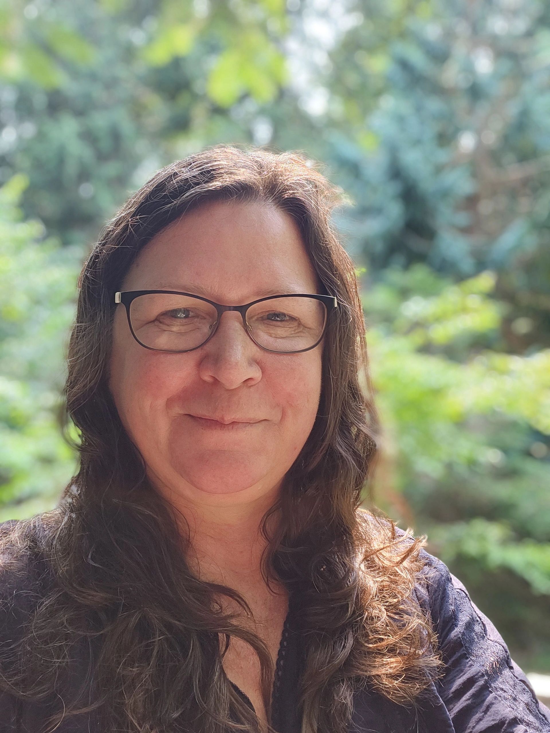 Smiling woman with glasses in outdoor natural setting.