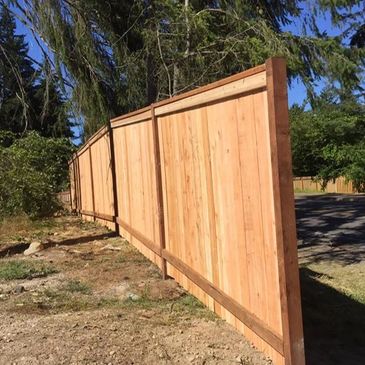 New wooden fence panels leaning unevenly along a grassy roadside.