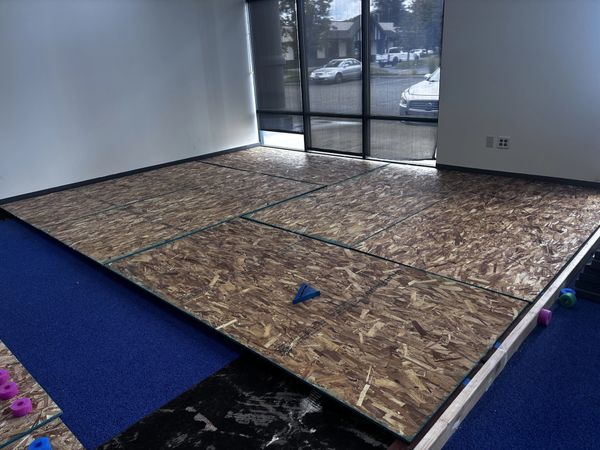 Wooden panels are laid out on a raised platform in a room with large windows.