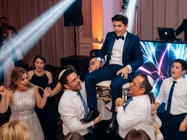 Guests lifting the guest of honor in a chair during a bar mitzvah celebration.
