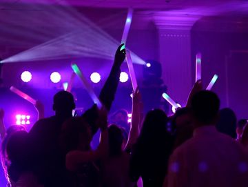 Dance floor, bathed in dynamic purple lighting and spotlights, with a crowd waving glowsticks.