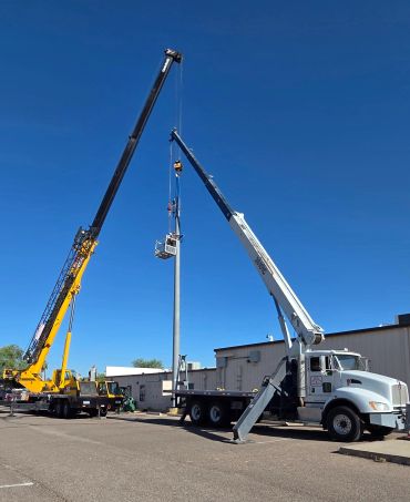 Two cranes lifting a pole with a basket under a clear blue sky.