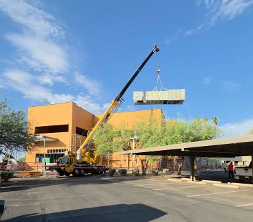 Crane lifting a large equipment unit at a construction site.