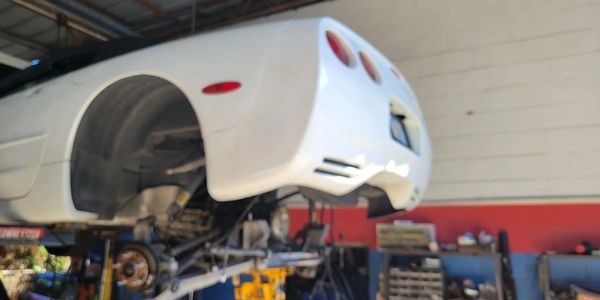 White car lifted in a garage without rear wheels.