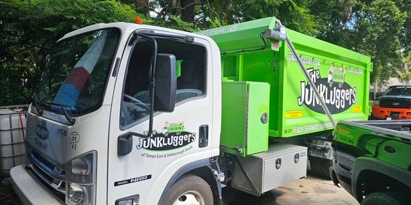 A white and green Junkluggers truck parked near trees.