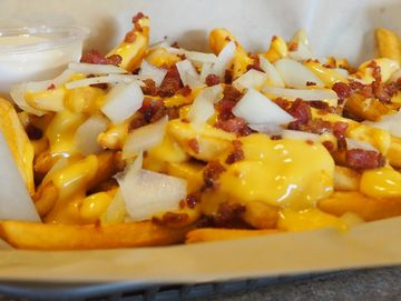 A mound of fries topped with nacho cheese, bacon, onion and sour cream
