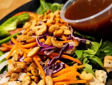A fresh salad of arugula, bright carrots and red cabbage with cashews and dressing.
