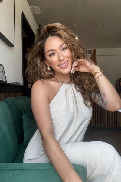 Smiling woman in white dress sitting on green couch indoors.