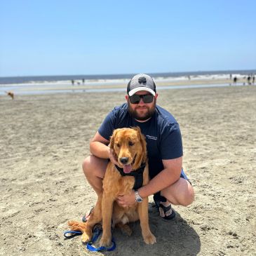 Man in sunglasses with dog on the beach.