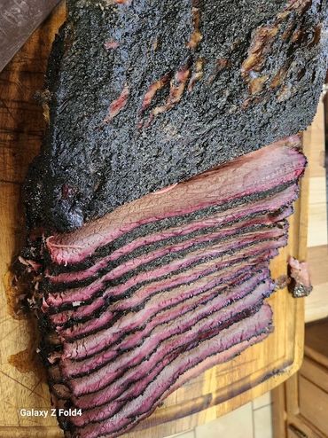 Sliced smoked brisket with a dark bark on a wooden cutting board.