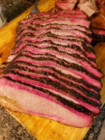 Sliced smoked brisket with a dark crust on a wooden cutting board.