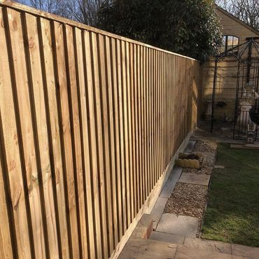 A wooden fence installation in a garden with a statue and greenery.