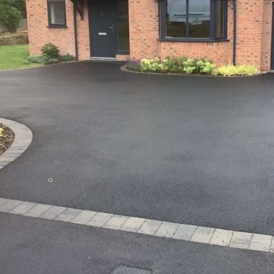 Newly paved asphalt driveway with brick edging in front of a brick house.