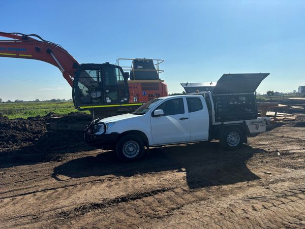 White utility truck with open tool compartments near an excavator on a sunny construction site.
