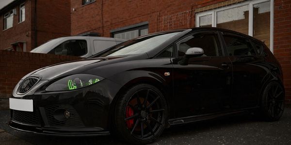 Black sporty hatchback car parked in a residential area with custom headlights.