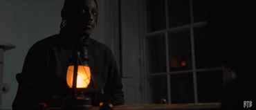 Man in dark room illuminated by a glowing lantern on the table.