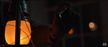 Gloved hand holding a vial near a glowing lantern in a dark setting.