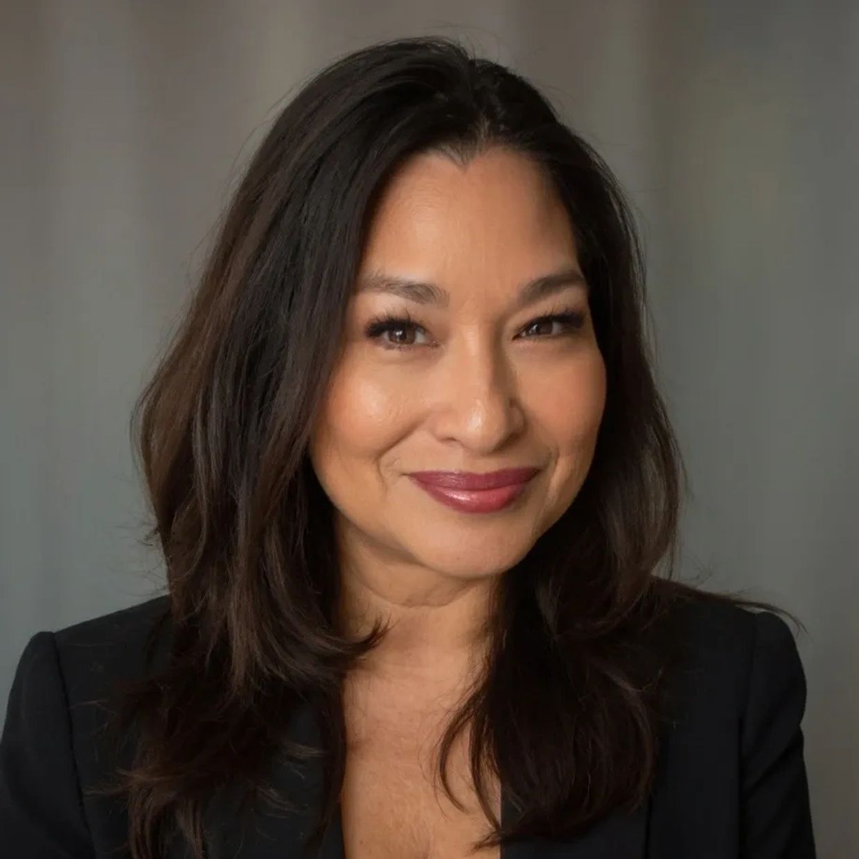 Smiling woman with dark hair in a black blazer against a neutral background.