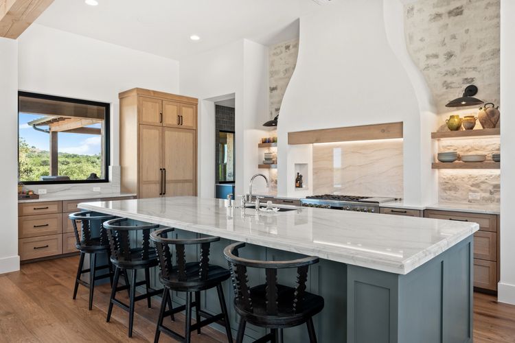 Modern kitchen with a large marble island and black chairs.