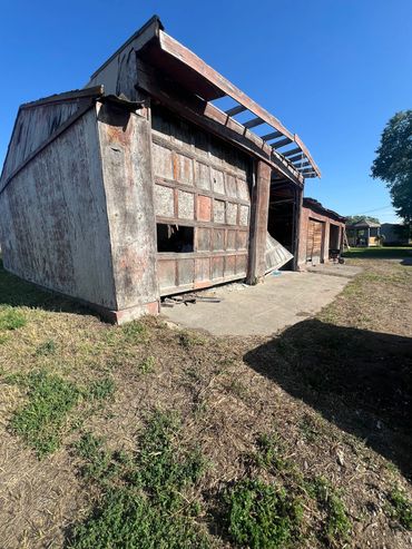 Dilapidated wooden garage with broken doors under clear blue sky.