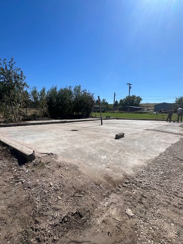 Concrete slab foundation with workers in the background on a clear day.