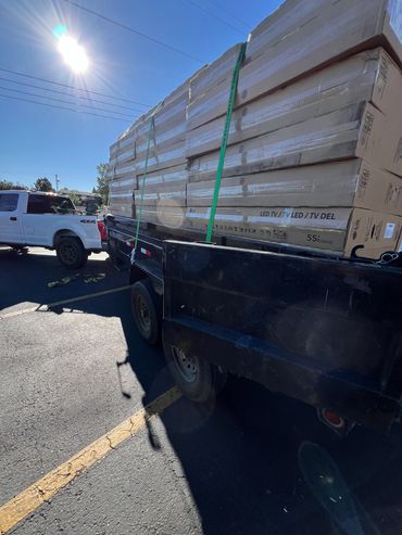 A trailer loaded with multiple 55-inch LED TV boxes under bright sunlight.