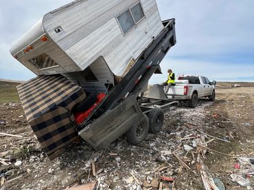 A person sitting on a white truck next to a tilted trailer at a dump site.
