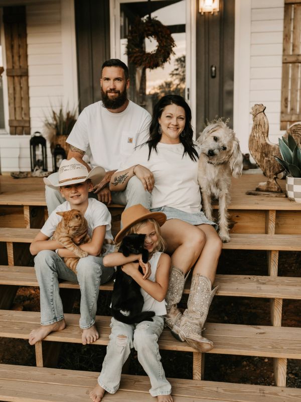 Family sitting on porch steps with pets and smiling.