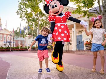 Children holding hands with Minnie Mouse at a theme park.