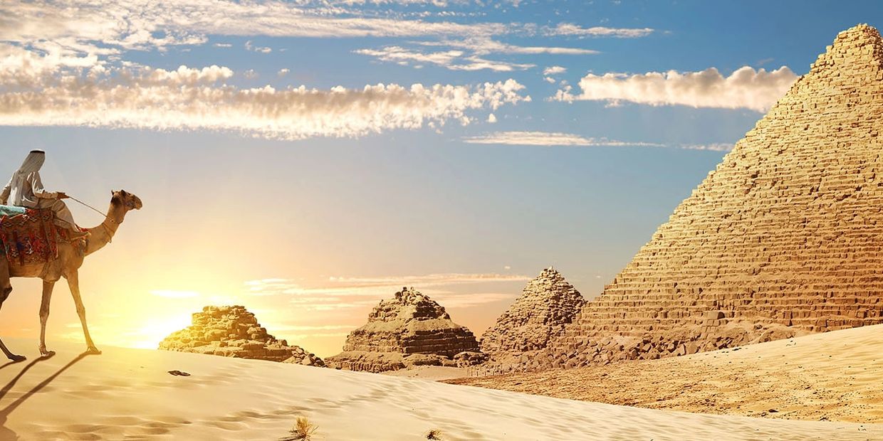 Camel rider near Egyptian pyramids at sunset.