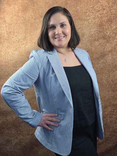 Woman in light blue blazer smiling against a textured brown background.