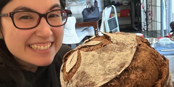 Happy woman showcasing a rustic, decorative loaf of bread.