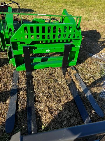 Close-up of green forklift tines on dry grass.