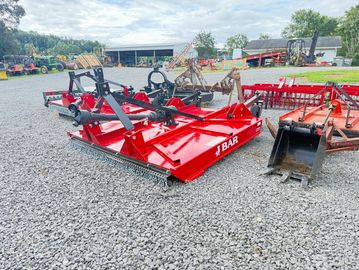 Red J Bar rotary mower on gravel with farming equipment around.
