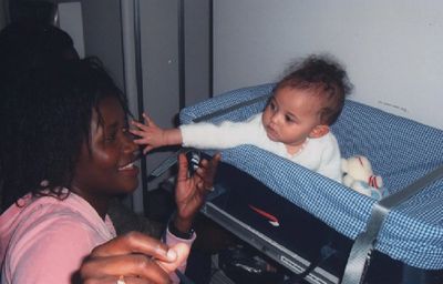 A baby joyfully reaching out to touch a smiling woman's face.