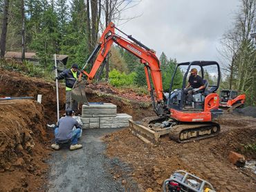 Workers using excavators to build a retaining wall with concrete blocks.