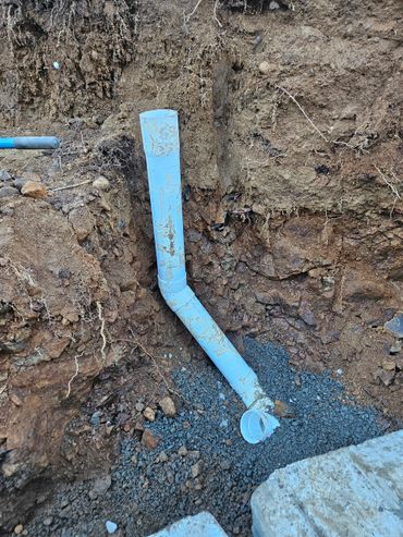 Blue PVC pipe installed in a dirt trench with gravel base.