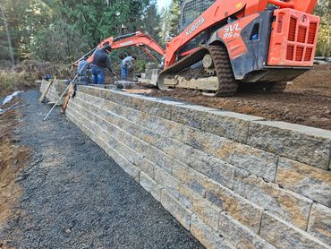 Construction workers building a stone retaining wall with heavy machinery.