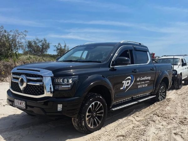 Black pickup truck with company logo on sandy terrain under blue sky.