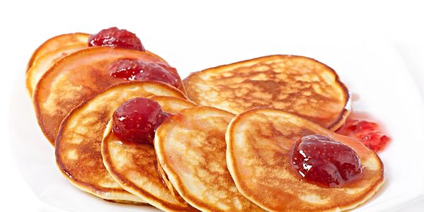 Stack of golden pancakes topped with dollops of strawberry jam on a white plate.