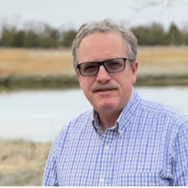 Man with glasses in a checkered shirt near water.