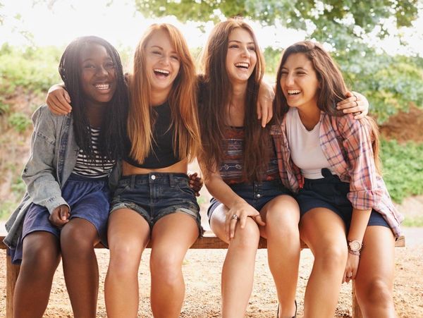 Four friends sitting on a bench, laughing together.