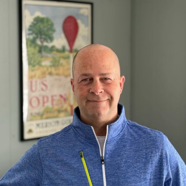 Smiling bald man in a blue zip-up sweater indoors.