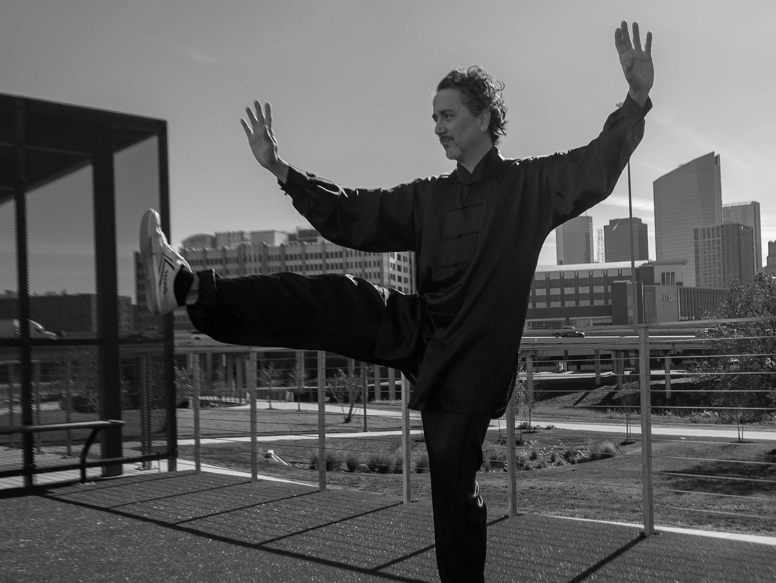 Tai chi pose kick right leg being performed with the downtown Houston skyline in background.